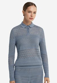 Ljusblå stickad långärmad polo med mönster, tre knappar, ribbad krage och manschetter. Texturerade sektioner skapar visuell kontrast.