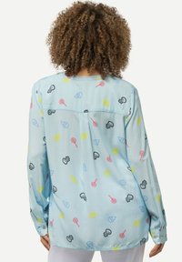 Blusa a maniche lunghe azzurro chiaro con fantasie giocose di caramelle e dolci in rosa, giallo, nero e blu. Tessuto morbido, vestibilità rilassata.