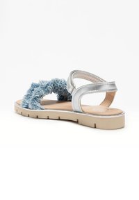 Sandali blu pelosi con cinturini in argento, suola piatta color beige, parte superiore testurizzata e design aperto. Presentano una banda larga e una fibbia regolabile.