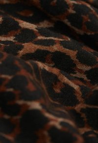 Close-up van zachte stof met een bruine en zwarte luipaardprint, waarbij de textuur en plooien zichtbaar zijn.