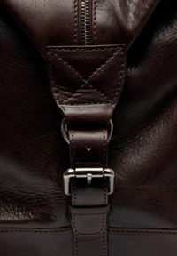 Sac en cuir marron avec fermeture éclair, matériel en acier inoxydable, une sangle en cuir matelassée et des coutures détaillées.