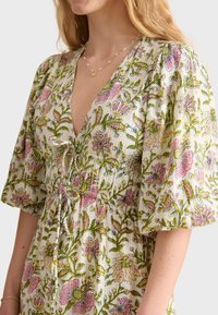 Robe fleurie avec un décolleté en V profond et des manches bouffantes amples. Fabriquée en tissu léger avec des motifs botaniques roses et verts.