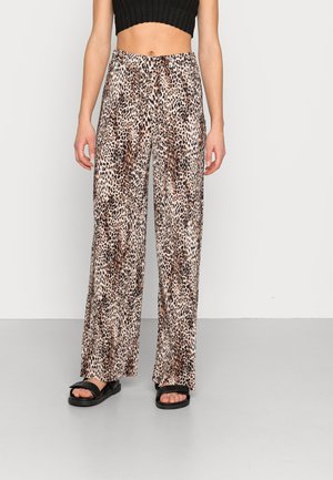 Vrouw draagt hooggetailleerde, wijde luipaardprintbroek, gecombineerd met een zwart cropped mouwloos topje en zwarte sandalen.