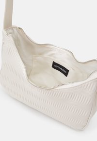 Tłoczona biała torba na ramię z zamknięciem na zamek i wyściółką z materiału. Wewnątrz znajduje się metka marki. Na zewnątrz torba ma falisty wzór.