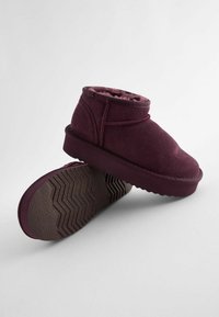 Bottines bordeaux en daim doux, avec une semelle en caoutchouc texturée à motif en zigzag et une doublure intérieure en peluche.