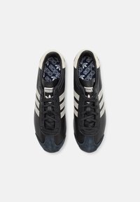 Mustad nahast tossud kolme valge triibuga, sinine nobedustipp, mustad paelad ja mustrilised sisetallad, millel on Adidas'i logo.