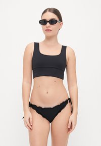 Crni bikini s gornjim dijelom s kvadratnim izrezom i donjim dijelom s volanom i vezanjem sa strane. Tkanina je glatka i rastezljiva, s elegantnim minimalističkim dizajnom.