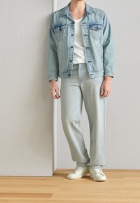 Ljusblå denimjacka med två bröstfickor, matchad med ljusblå jeans. Vit t-shirt under och ljusa sneakers.