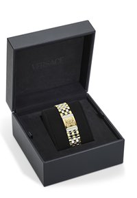 Reloj en tonos dorado y plateado exhibido en una caja negra. Presenta un emblema de león en una esfera rectangular y una pulsera de eslabones con un patrón geométrico.