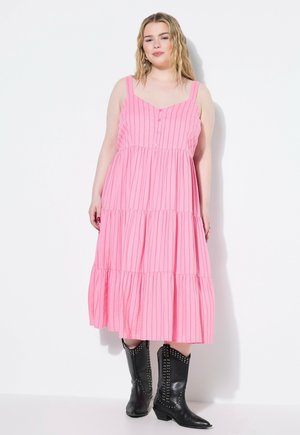 Robe maxi à volants rose avec des rayures verticales, dotée de bretelles ajustables et de boutons à l'avant, associée à des bottes de cow-boy noires à clous.