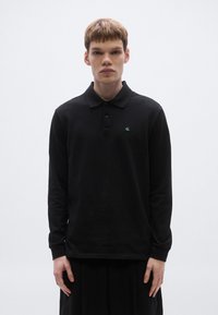 Mustast puuvillast pikkade varrukatega polo särk. Rinna peal roheline logo, krae juures kaks nuppu ja soonikkoes varrukasuu.