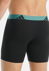 Černé sportovní boxerky s tyrkysovým páskem a černými akcenty loga Adidas, s hladkou texturou. Design je přiléhavý a moderní.