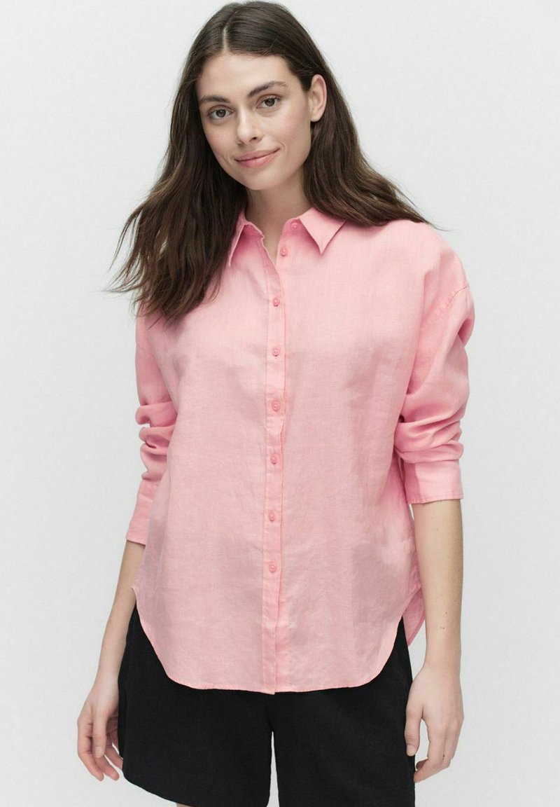 Lichtroze lange mouw blouse van linnen, met een knoopsluiting aan de voorkant, een puntkraag en een ontspannen pasvorm, gecombineerd met zwarte shorts.