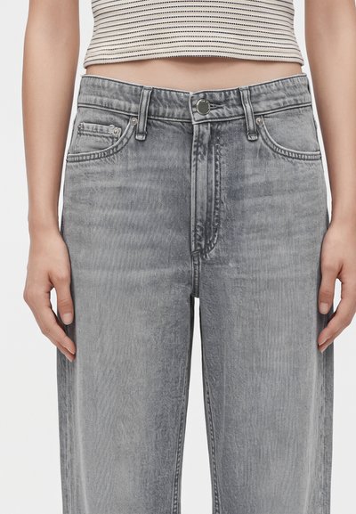 Gros plan d'une personne portant un jean gris délavé taille haute et un top court rayé noir et blanc, montrant son ventre et ses mains.
