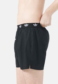 Svarta atletiska shorts med elastisk midja och vita tre-stripes logotypdetaljer. Lättviktsmaterial och sidospalter för rörlighet.