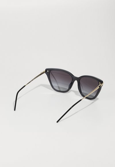 Ochelari de soare din plastic negru cu lentile gradient, formă unghiulară de cat-eye, accente aurii din metal pe temple și brațe subțiri negre.