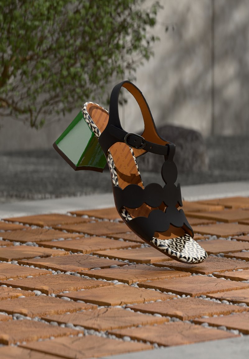 Μαύρο σανδάλι με ανοιχτά δάχτυλα και γεωμετρικό σχέδιο με κοψίματα, διαθέτει πράσινο τακούνι σε σχήμα μπλοκ και σωληνωτό εσωτερικό πέλμα με σχέδιο. Περιλαμβάνει ρυθμιζόμενο λουράκι στον αστράγαλο.