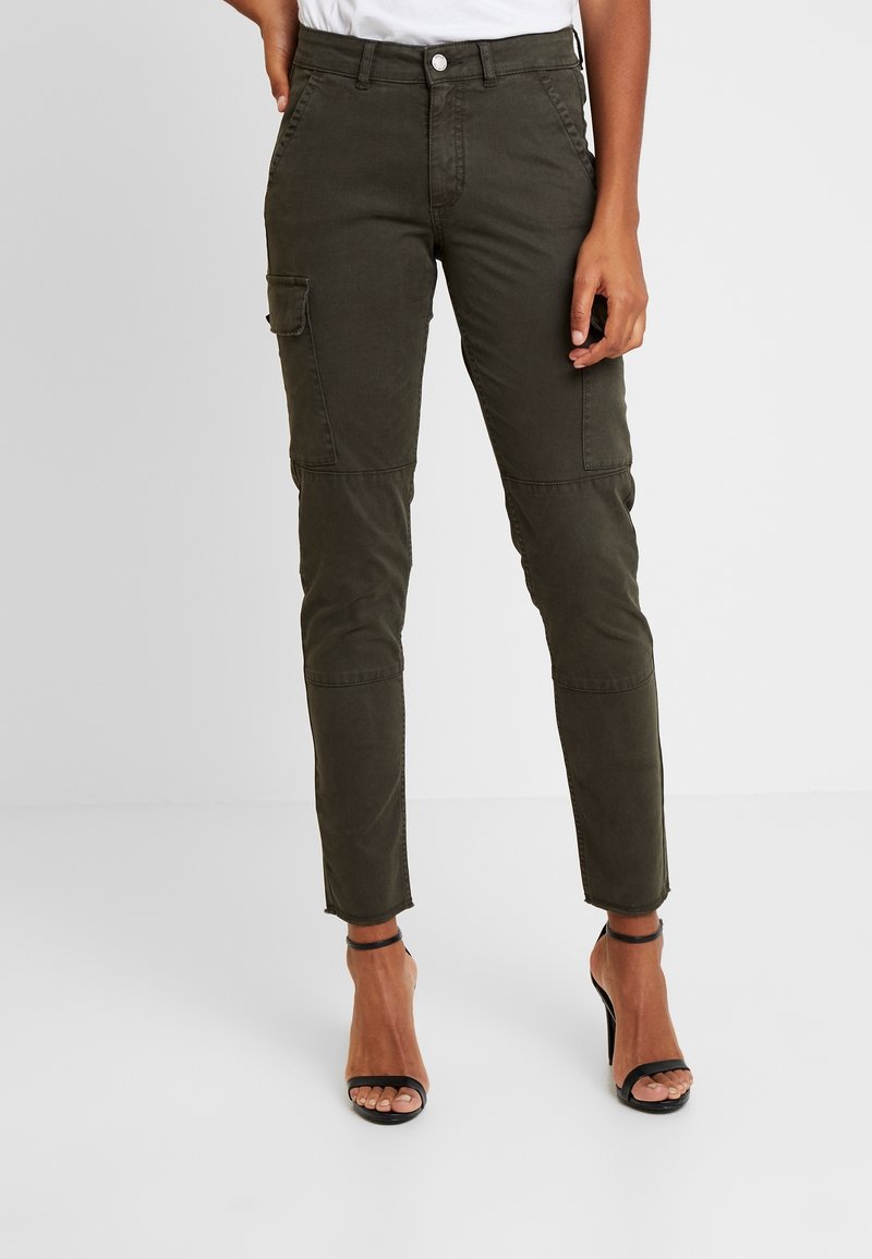 Pantalons cargo vert olive avec poches latérales, coupe ajustée, jambes fuselées et ourlets roulés, fabriqués en tissu doux et résistant. Associés à des talons noirs.