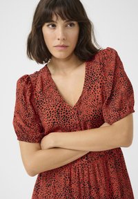 Robe rouge avec imprimé léopard noir, manches courtes bouffantes, décolleté en V profond, taille froncée et jupe fluide. Texture du tissu lisse.