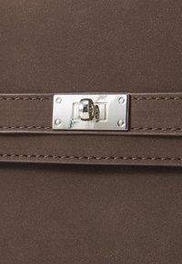 Sac en cuir brun texturé avec une sangle horizontale et un fermoir rectangulaire argenté à fermeture tournante en vue rapprochée.