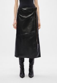 Mustat nahka midi-hameet, joissa on sileä pinta, sivuhalkiot ja solk yksityiskohta. Edessä kontrastiväriset ompeleet.