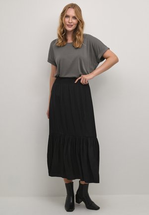 Grijs shirt met korte mouwen gecombineerd met een zwarte gelaagde maxi rok. De rok heeft een geraffineerde tailleband en vloeiend stof. Zwarte enkellaarsjes.