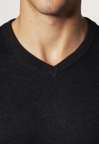 Pull bleu marine à col en V avec une texture côtelée et une coupe ajustée, présentant un col sans coutures et un matériau doux et léger.