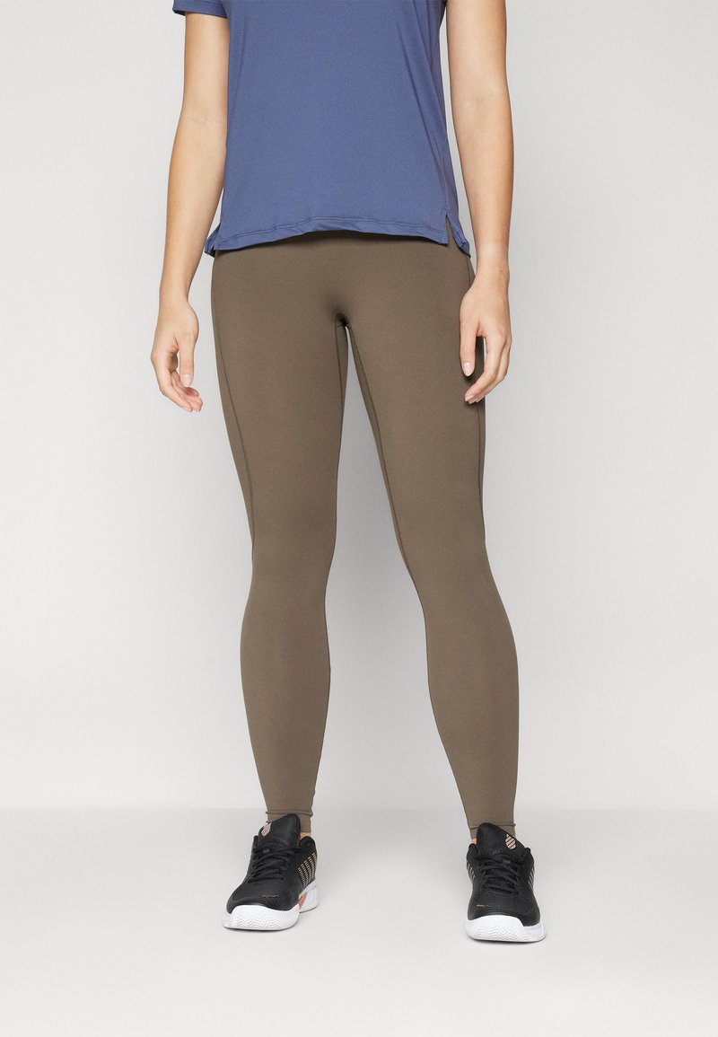 Barna leggings rugalmas anyagból, sima felülettel és testhezálló fazonnal, kék, rövid ujjú toppal és fekete cipővel párosítva.