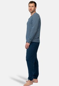 Gestreepte navy top met lange mouwen en witte strepen, gecombineerd met effen navy broek. Stof lijkt zacht; de broek heeft een omslagdetail aan de zoom.