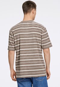 Brun og creme stribet kortærmet t-shirt, bl�ød tekstur, afslappet pasform, rund halsudskæring, synlig syning ved kanten, båret med blå jeans.
