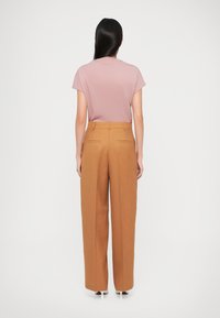 Un haut rose clair à manches courtes associé à un pantalon large taille haute de couleur marron chaud. Le pantalon est muni de deux poches arrière.
