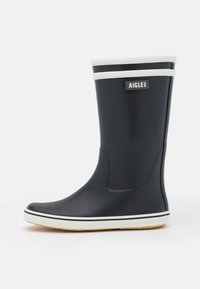Botte de pluie en caoutchouc noir avec des accents blancs en haut et sur la semelle, présentant une pointe arrondie et une surface texturée pour l'adhérence. Étiquette de la marque visible.