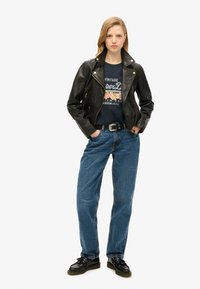 Giacca biker in pelle nera, maglietta grafica blu con design floreale, jeans blu a vita alta e scarpe nere con lacci.