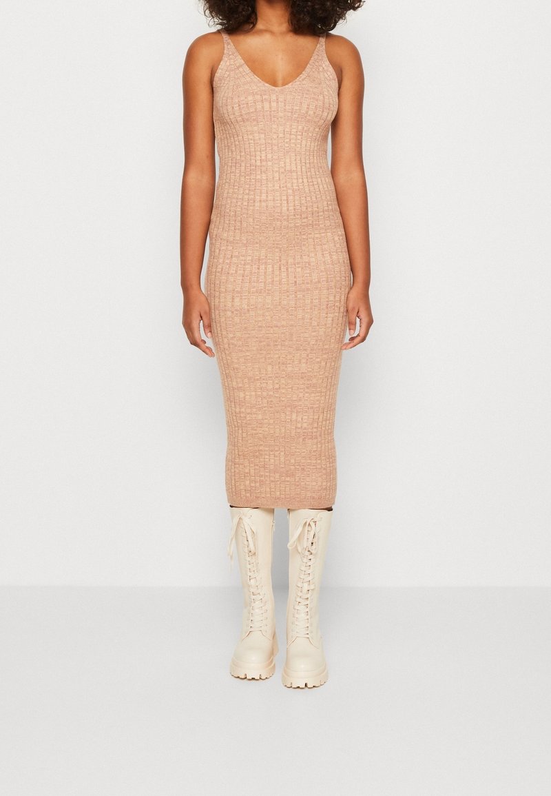 Robe bodycon en tricot couleur beige clair avec un motif texturé et un col en V. Associée à des bottes montantes crème à lacets.