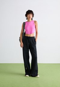 Rosa, kurz geschnittenes Tanktop mit einem runden Halsausschnitt, kombiniert mit lockeren schwarzen Sweatpants, die ein Logo und einen Kordelzug haben. Texturiert schwarze Tasche.