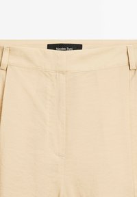 Beige byxor med en slät yta, med rak passform, framfickor och en märkessvart etikett på midjebandet.
