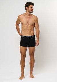 Črne bokserice iz mehkega materiala, z elastičnim pasom z logotipom U.S. Polo Assn., ki se tesno prilegajo in imajo gladko teksturo.