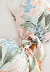 Haut de bikini en tissu à motif floral dans des couleurs pastel avec des feuilles vertes et des fleurs bleues, présentant un nœud noué au centre devant.