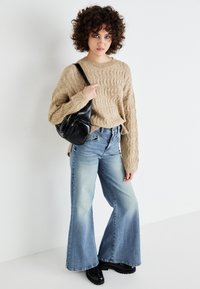 Beige kabelstrikket genser med løs passform, kombinert med lyseblå vide jeans og svart crossover-veske, brukt med blanke svarte støvler.