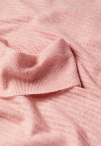 Pehmeä vaaleanpunainen ribbineulos, jossa on teksturoitu pinta, ja jossa on lempeitä taitoksia ja ryppyjä, jotka korostavat materiaalin pehmeyttä ja lämpöä.