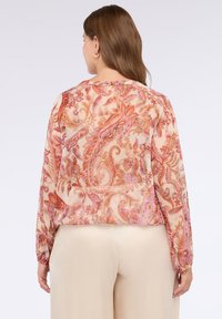 Lehká, průsvitná blůza s pastelovým květinovým a paisley vzorem v odstínech růžové a oranžové, dlouhými rukávy a zaobleným lemem.