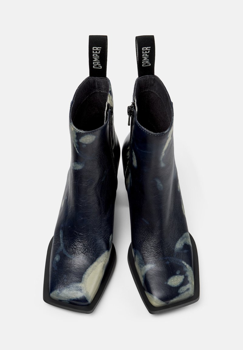 Marina ank stövlar med ett mönstrat läderövre, fyrkantig tå, svarta sidodragkedjor och öglade dragflikar som visar "CAMPER."