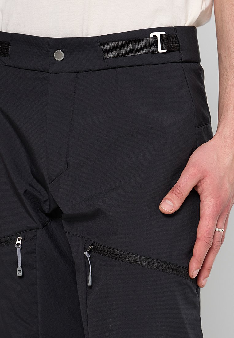 Schwarze Hose aus strukturiertem Stoff, mit Gürtelschlaufen und zwei seitlichen Reißverschluss-Taschen mit kontrastierenden Reißverschluss-Zippern.