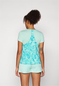 Uma t-shirt atlética turquesa de mangas curtas apresenta um design texturizado nas costas, complementada por calções combinantes, ambos em cores semelhantes.