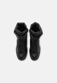 Botas negras de cordones con un upper acolchado, que presentan un exterior de cuero liso y un forro texturizado. Altura por la mitad de la pantorrilla, diseño de punta redonda.