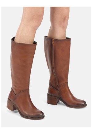 Bruine leren kniehoge laarzen met blokhakken en zijrits, gedragen op blote benen, tegen een witte achtergrond.