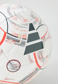 Biela futbalová lopta s červenými a čiernymi akcentmi, textúrovaným povrchom, geometrickými vzormi a potlačou značky v kontrastných farbách.