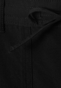 Gros plan sur un tissu noir avec des coutures visibles et un cordon noir lâche enroulé autour de la couture.