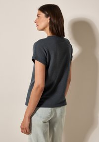 Mørkegrå tekstureret kortærmet top med rund halsudskæring. Designet har en afslappet pasform og er parret med lyse denim bukser.