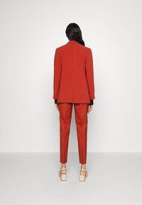 Czerwona, dopasowana marynarka i pasujące do niej wąskie spodnie wykonane z gładkiego materiału. Charakteryzują się pojedynczym rozcięciem i minimalistycznym designem, zestawione z masywnymi szpilkami.